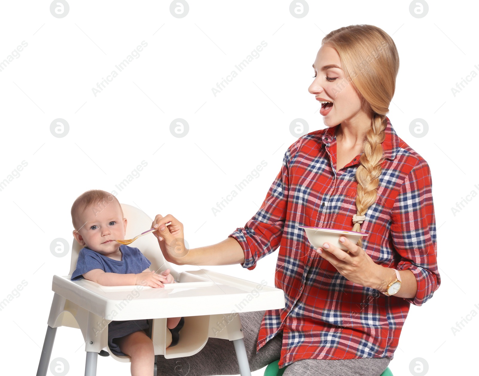 Photo of Woman feeding her child in highchair against white background. Healthy baby food