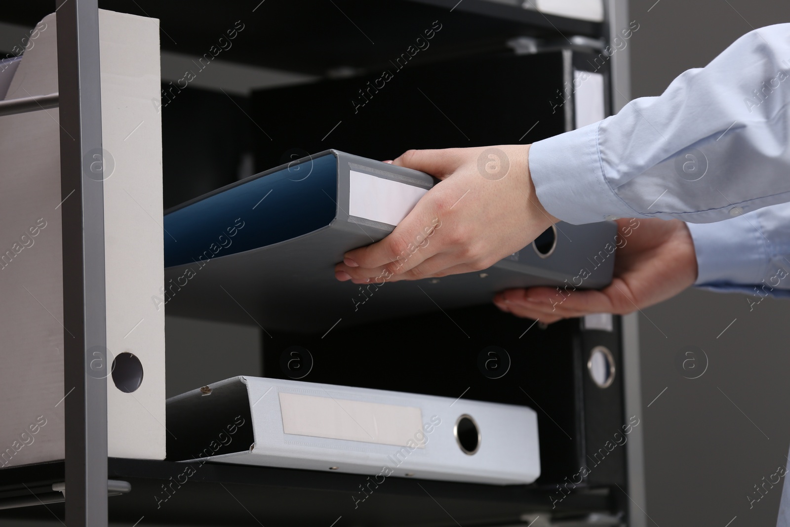 Photo of Woman taking folder with documents from shelf in office, closeup