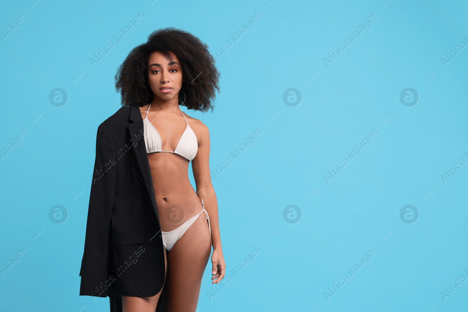 Photo of Beautiful woman in stylish bikini and jacket on light blue background, space for text