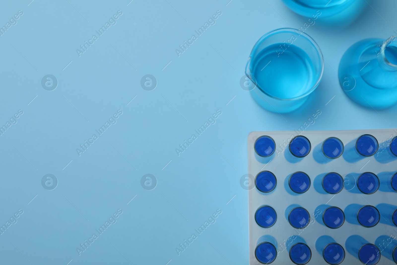 Photo of Laboratory glassware with light blue liquid on turquoise background, flat lay. Space for text