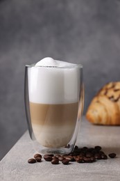 Photo of Aromatic latte macchiato in glass, coffee beans and croissant on light grey table