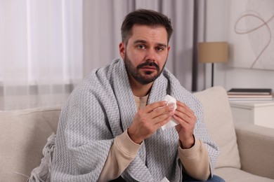 Photo of Sick man wrapped in blanket with tissue on sofa at home. Cold symptoms