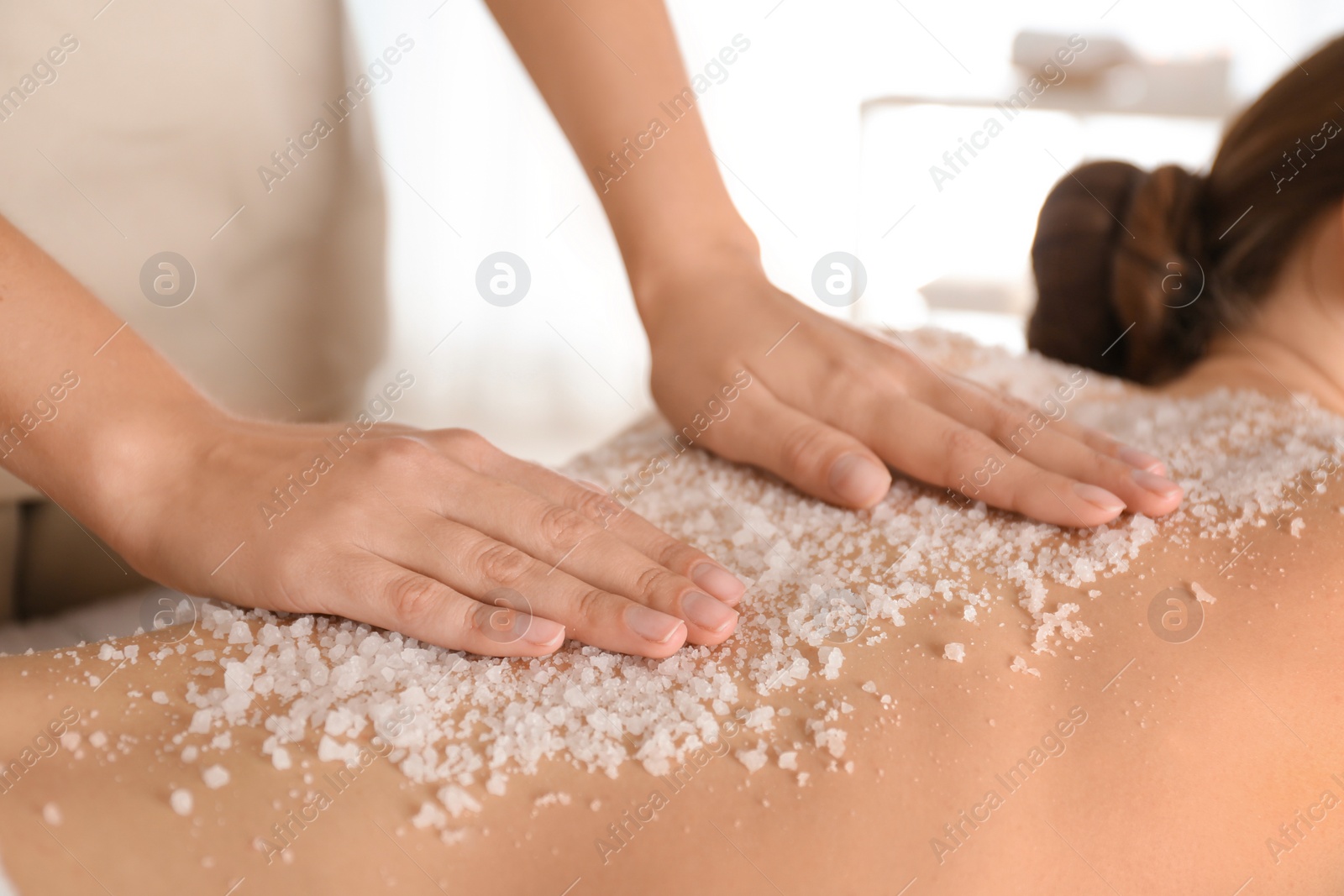 Photo of Young woman having body scrubbing procedure with sea salt in spa salon, closeup