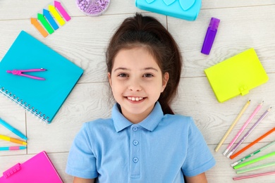 Cute little girl with school stationery on wooden background, top view