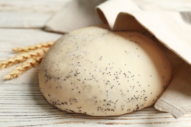 Photo of Raw dough with poppy seeds under towel on wooden table