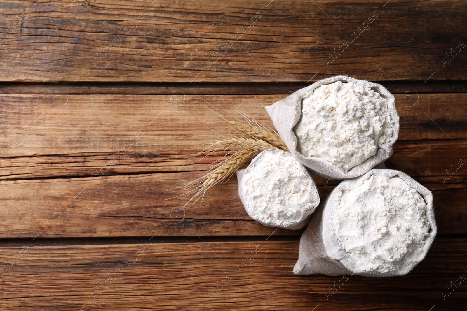 Photo of Sacks with flour and wheat spikes on wooden background, flat lay. Space for text