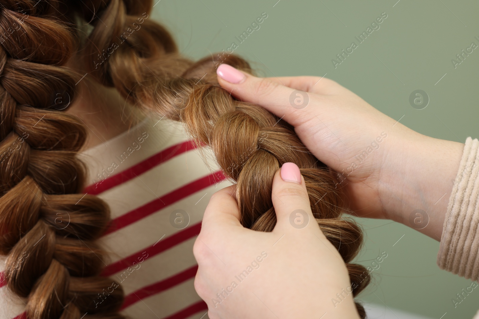 Photo of Professional stylist braiding woman's hair on olive background, closeup