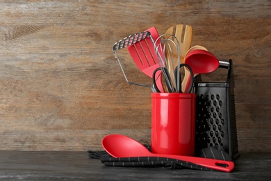 Photo of Holder with kitchen utensils on table against wooden background. Space for text