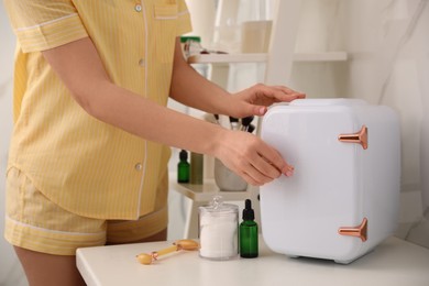 Woman opening cosmetic refrigerator in bathroom, closeup