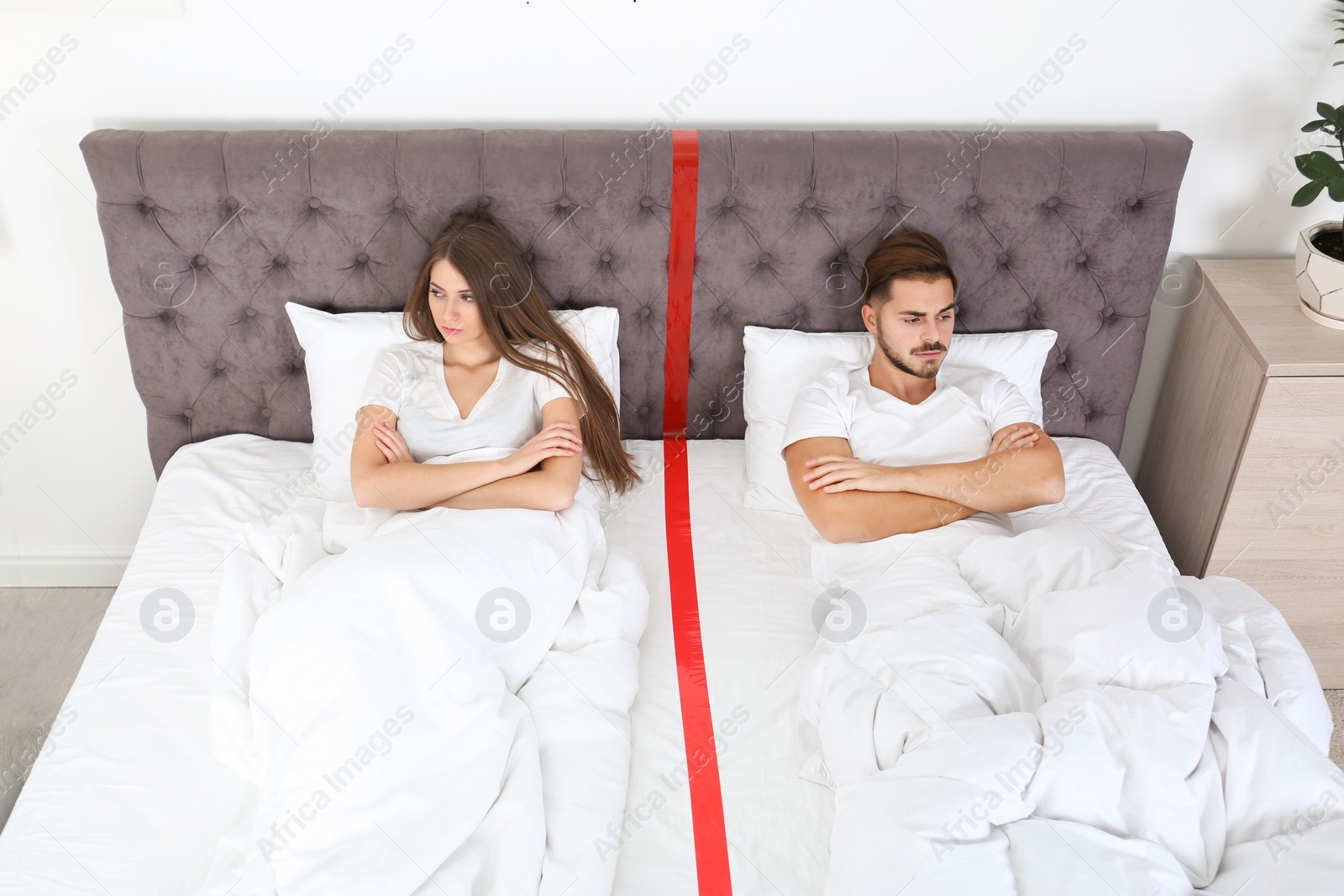 Photo of Upset young couple with relationship problems lying separately in bed at home