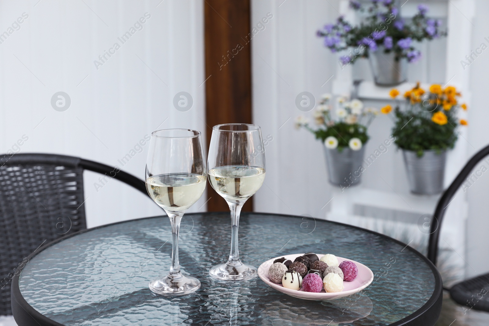 Photo of Glasses of wine and candies on glass table on outdoor terrace