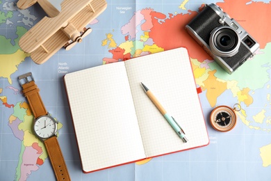 Flat lay composition with notebook and camera on world map, space for text. Travel agency