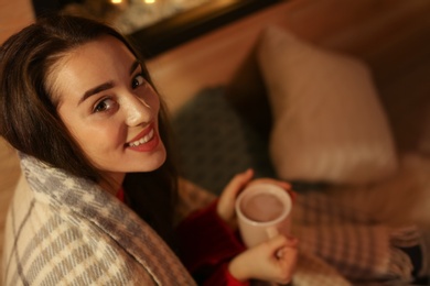 Photo of Young woman with plaid drinking coffee at home. Winter season