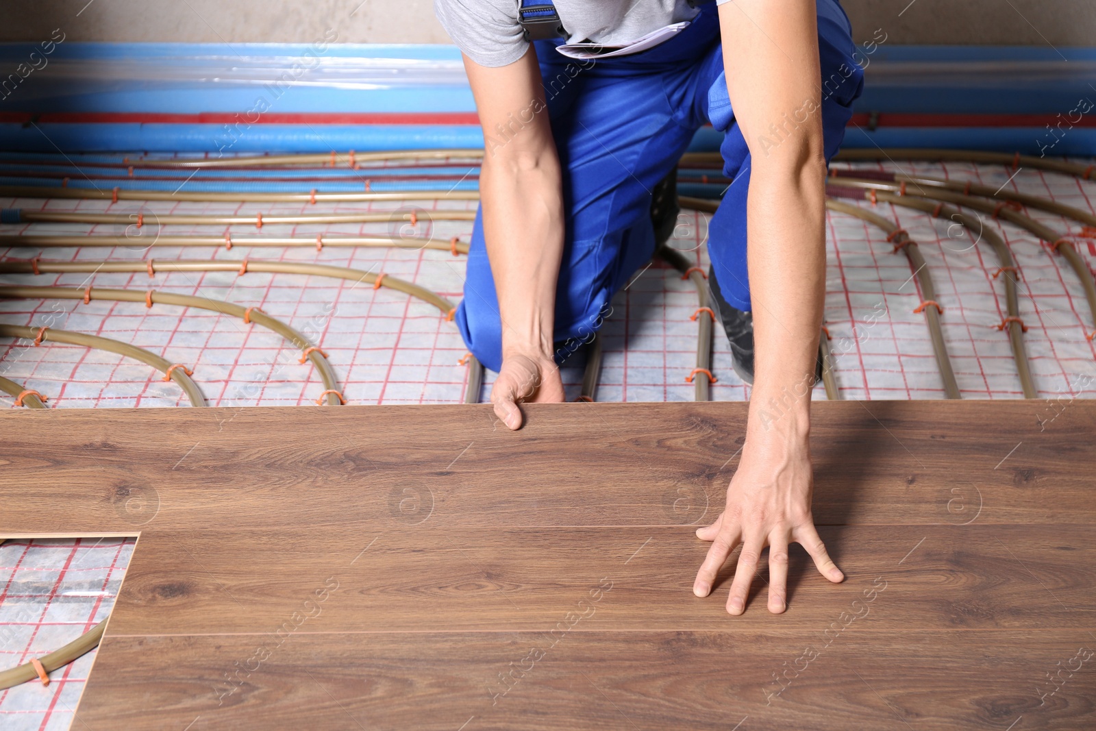 Photo of Worker installing new wooden laminate over underfloor heating system, closeup