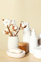 Different bath accessories and cotton flower on wooden table against beige background