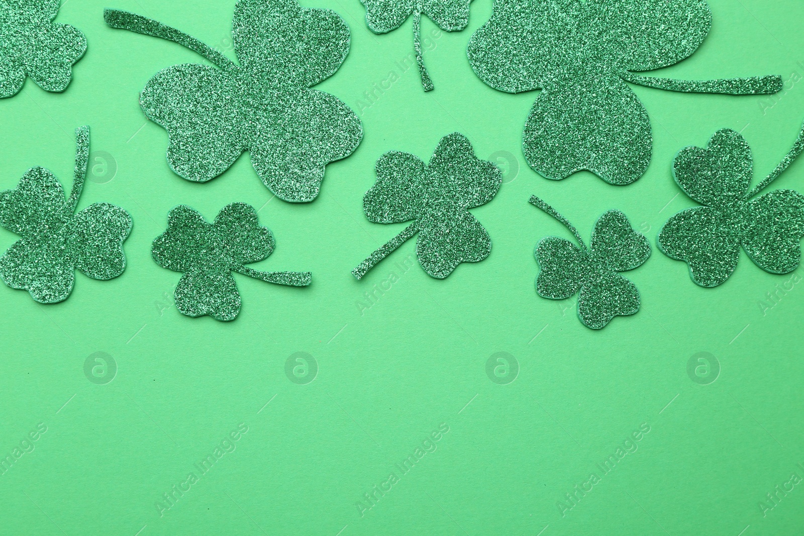 Photo of St. Patrick's day. Shiny decorative clover leaves on green background, flat lay. Space for text