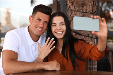 Photo of Lovely couple taking selfie after they got engaged in outdoor cafe