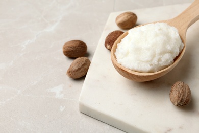 Shea butter in wooden spoon and nuts on table. Space for text