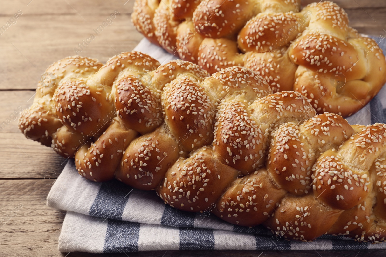 Photo of Homemade braided breads with sesame seeds on wooden table, closeup. Challah for Shabbat