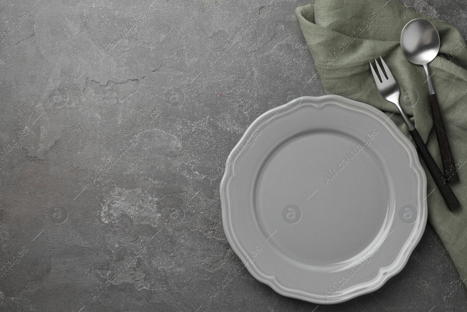 Photo of Stylish setting with cutlery, napkin and plate on grey textured table, top view. Space for text