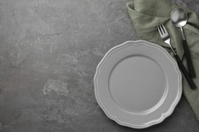 Stylish setting with cutlery, napkin and plate on grey textured table, top view. Space for text