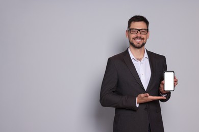 Smiling man in suit showing smartphone on light grey background. Space for text