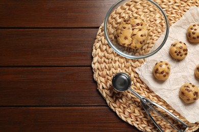 Photo of Fresh dough and uncooked chocolate chip cookies on wooden table, top view. Space for text