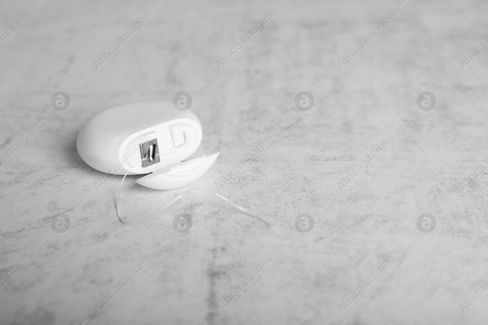 Photo of Container with dental floss on light grey textured table. Space for text