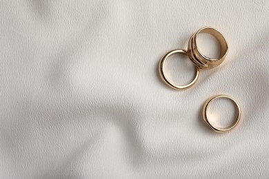 Photo of Elegant golden rings on white fabric, flat lay with space for text. Stylish bijouterie