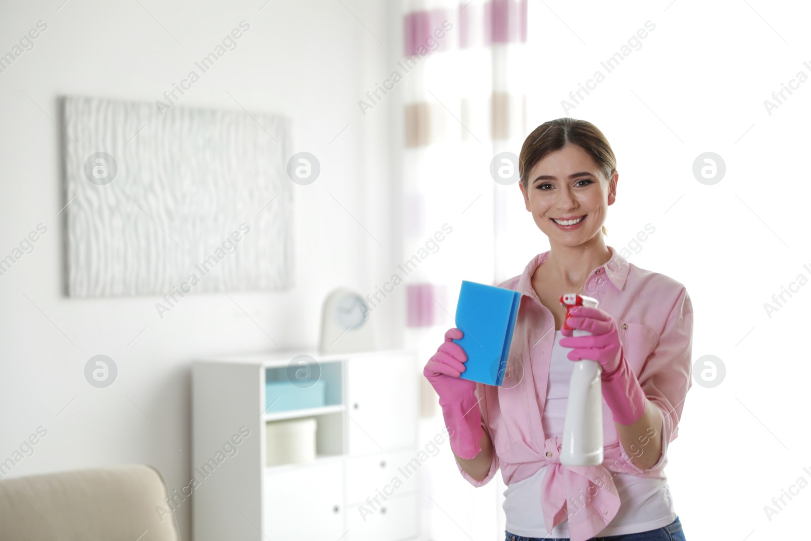 Photo of Happy woman in gloves with cleaning product and sponge at home. Space for text