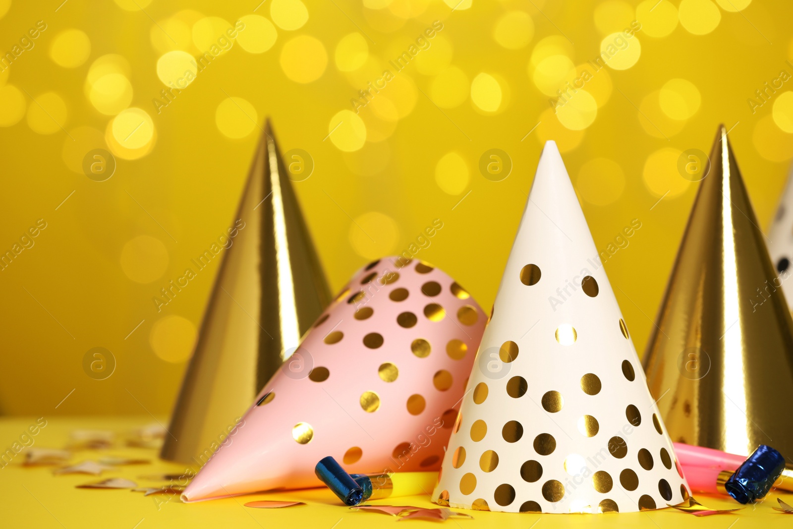 Photo of Party hats and festive items on table against yellow background with blurred lights