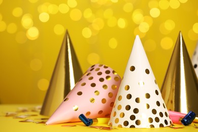 Party hats and festive items on table against yellow background with blurred lights