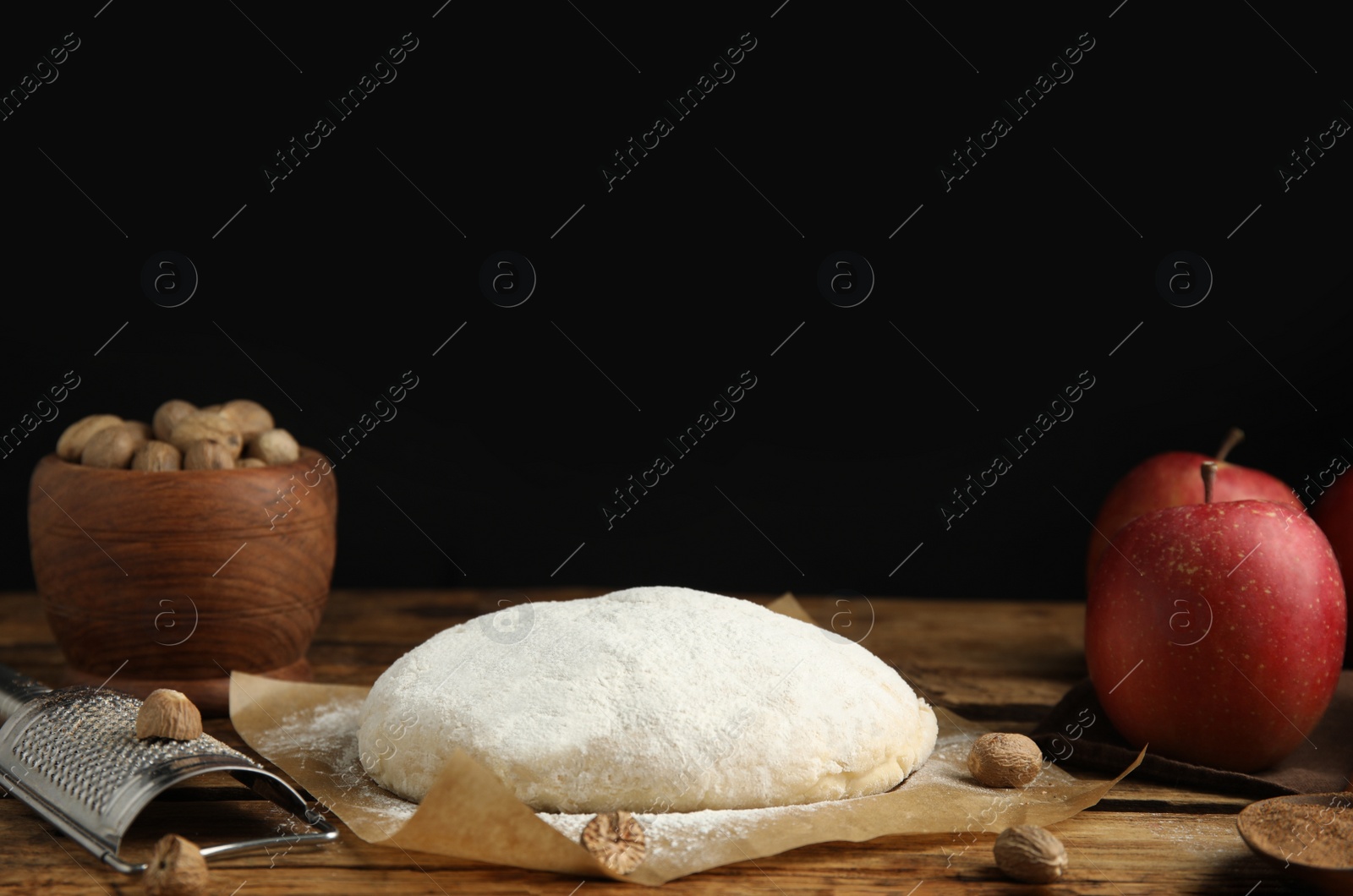 Photo of Raw dough, nutmeg seeds and apples on wooden table against black background, space for text