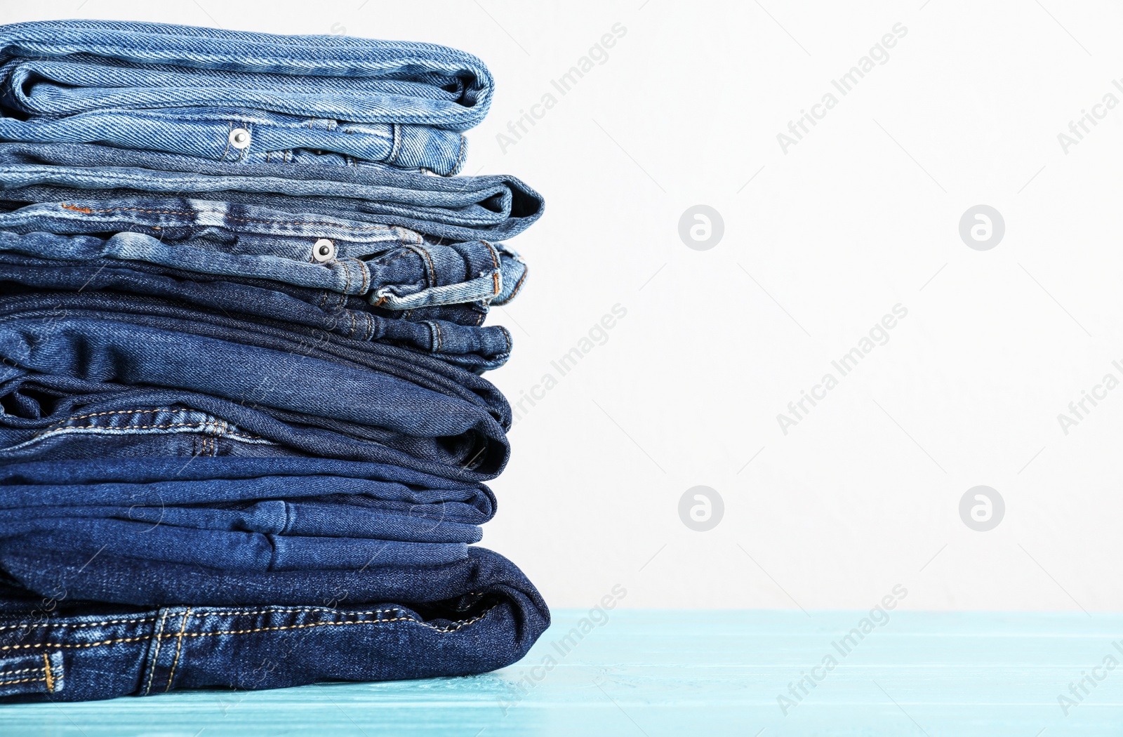 Photo of Stack of different jeans on blue wooden table. Space for text