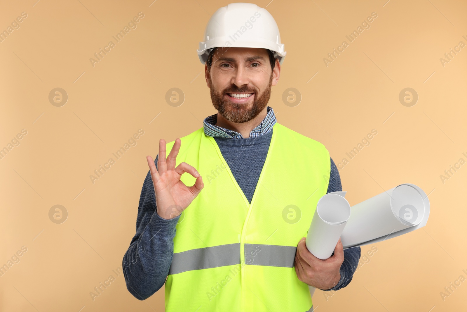 Photo of Architect in hard hat with drafts showing OK gesture on beige background