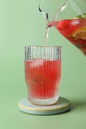 Photo of Pouring tasty summer watermelon drink with lime from jug into glass on pale light green background