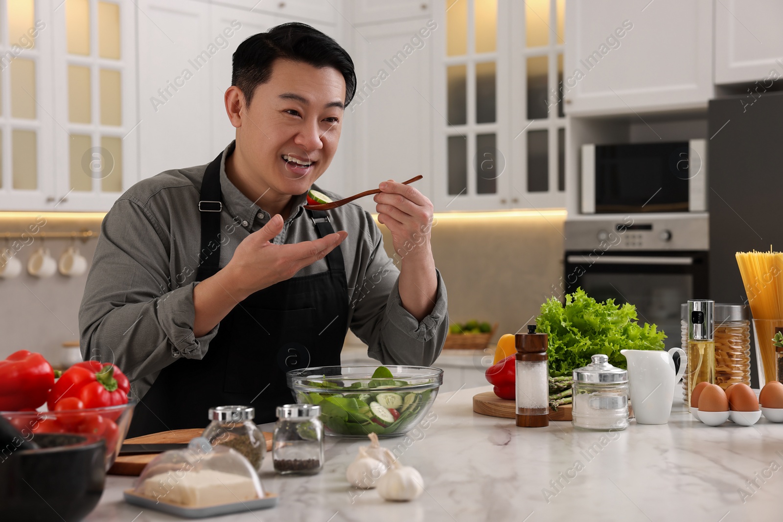 Photo of Cooking process. Man tasting salad in kitchen