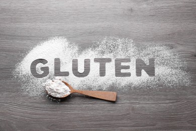 Photo of Word Gluten written with flour and spoon on wooden table, flat lay