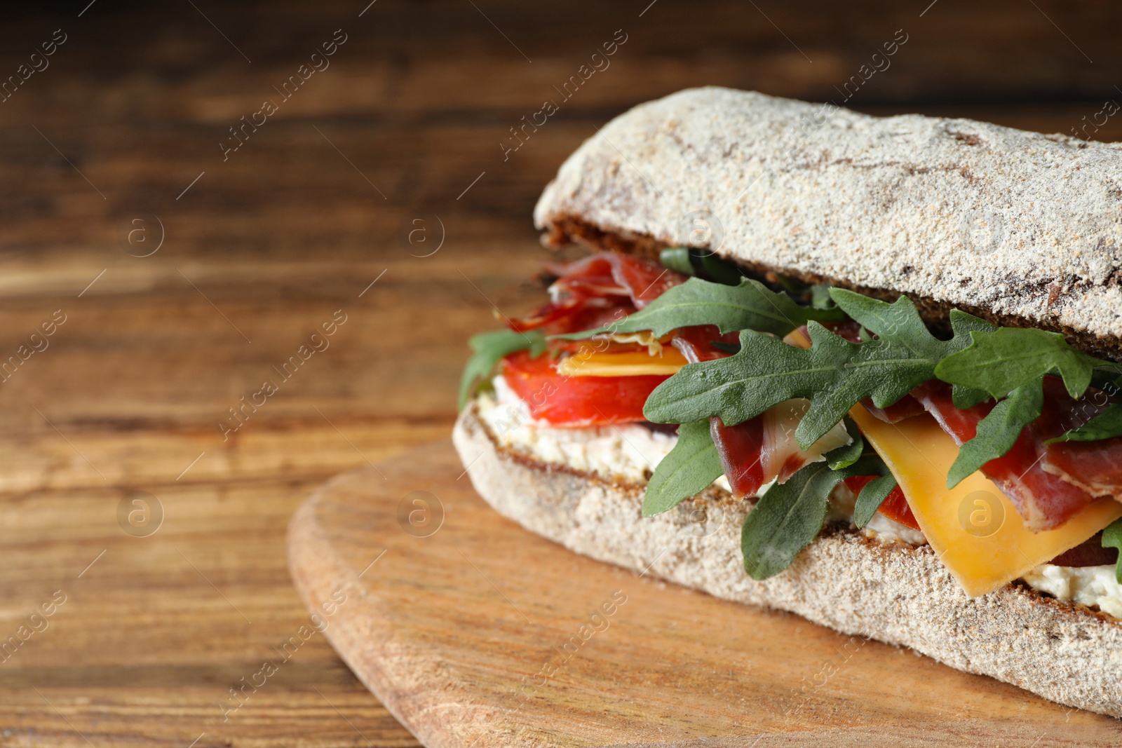 Photo of Delicious sandwich with fresh vegetables and prosciutto on wooden table, closeup. Space for text