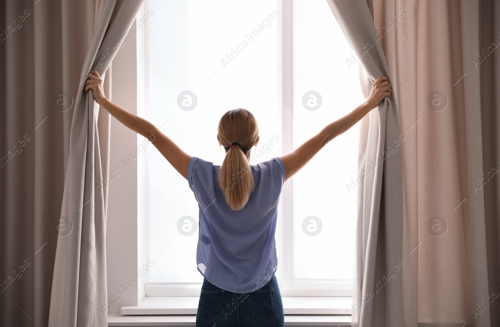 Photo of Woman opening curtains and looking out of window at home