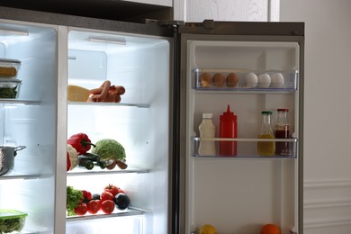 Photo of Open refrigerator full of different products in kitchen