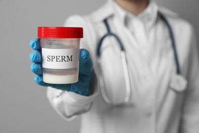 Photo of Doctor holding container with sperm on grey background, closeup. Space for text