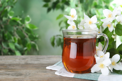 Photo of Cup of tea and fresh jasmine flowers on wooden table. Space for text