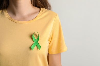 Photo of Woman with green ribbon on t-shirt against light background. Cancer awareness
