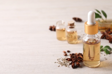 Photo of Bottles of essential oil, anise and seeds on white wooden table. Space for text