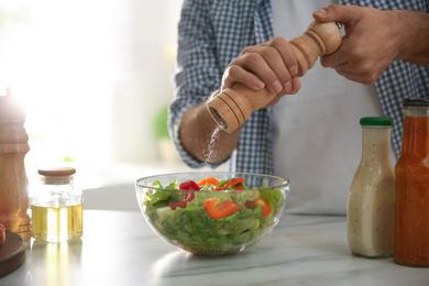 Photo of Man cooking salad at table in kitchen, closeup