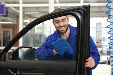 Worker cleaning automobile window glass with rag at car wash