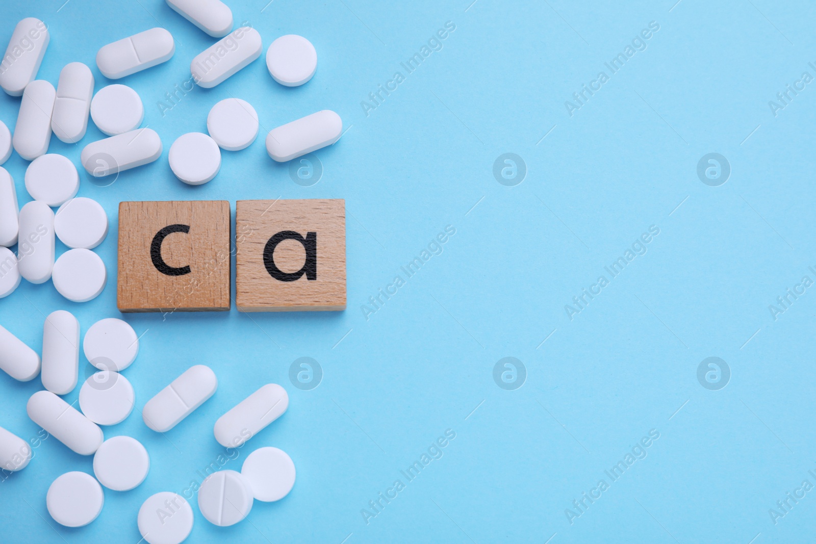 Photo of Wooden cubes with symbol Ca (Calcium) and pills on turquoise background, top view. Space for text