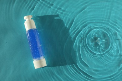 Photo of Bottle of cosmetic product in water on turquoise background, top view. Space for text