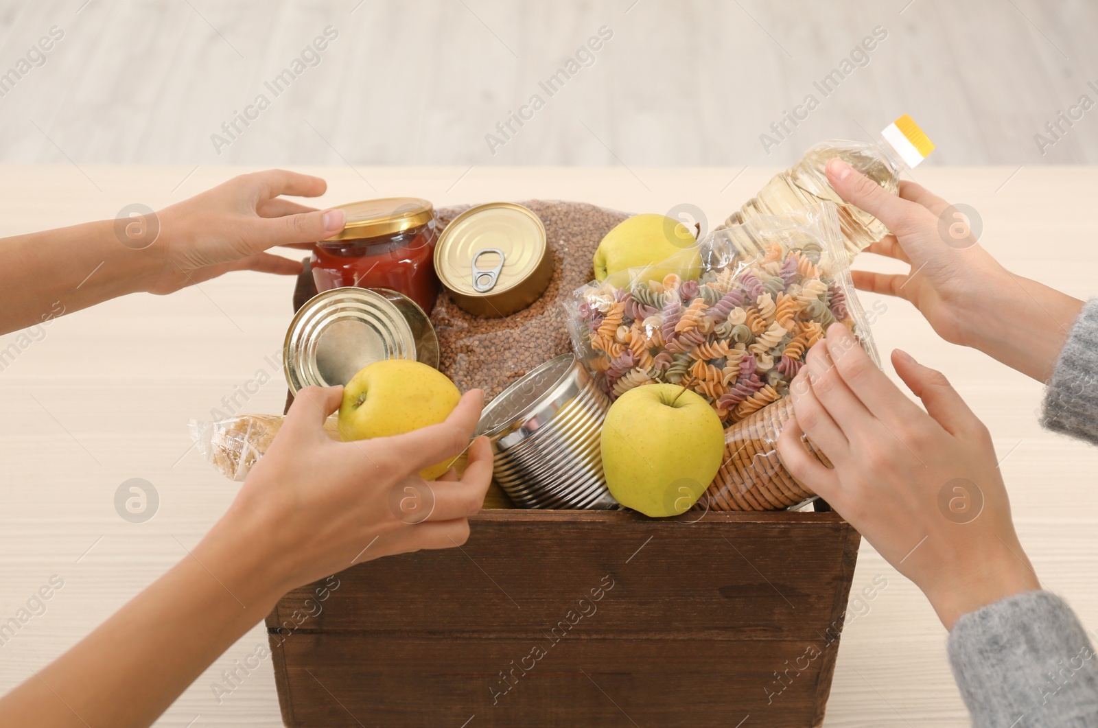 Photo of Women taking food out of donation box on wooden table, closeup